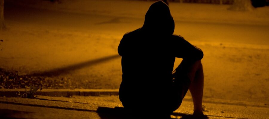 A youth sits on the floor with his hood up